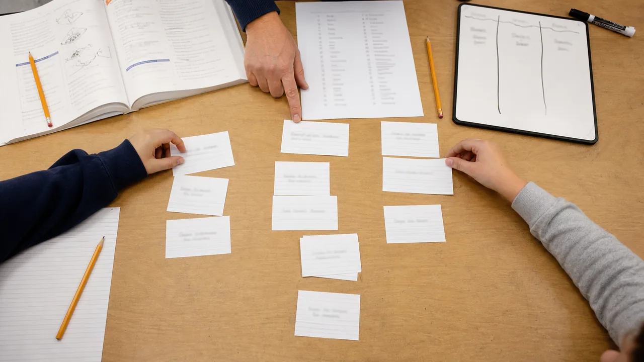 Students sorting science vocabulary cards beside a class workbook and word list